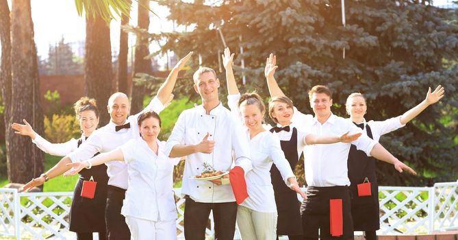 A large group of happy and emotional waiters standing in a row behind each other are happy to raise their hands up