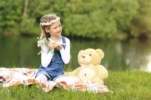 little girl with a soft toy on a picnic near the river on a Sunny day
