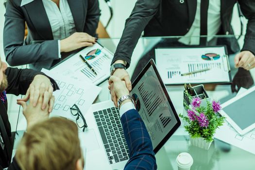 handshake of business partners on the background of financial graphs lying in the workplace