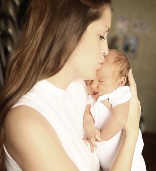 serene newborn baby in his mother's arms on the background of children's room