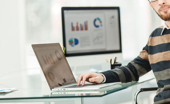 Finance specialist working on laptop with financial charts and marketing schemes in the modern office