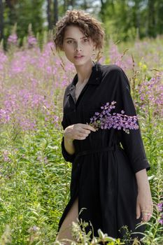 Young woman with a bouquet of lupines in her hand against the background of blooming Ivan-tea. Soft selective focus