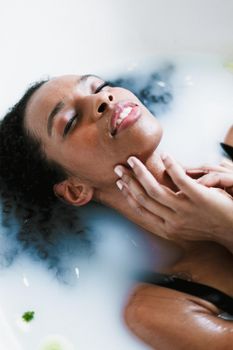 Young beautiful afro american girl taking bath and lying in foam, wearing swimsuit. Concept of relax and