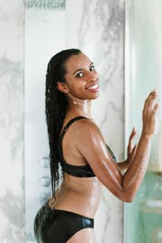 Afro american woman standing in bathroom with wet hair and wearing swimsuit. Concept of personal care and relax.