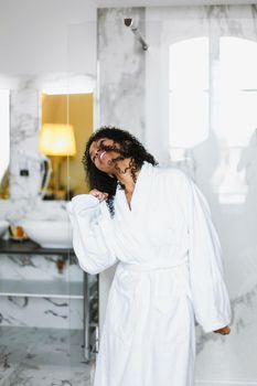 Young afro american girl dancing in bathroom and wearing white bathrobe. Concept of female person and relax, leisure and personal care.