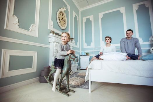 happy little girl swinging on a wooden horse in the bedroom of their parents