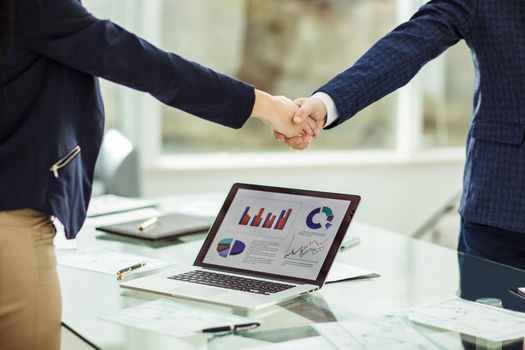 in the foreground is shaking hands with financial partners near the workplace in the modern office
