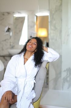 Young happy afro american woman wearing bathrobe and sitting in bathrom.