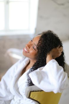 Portrait of afro american woman sitting in bathroom and wearing bathrobe. Concep of spa and morning hygiene.