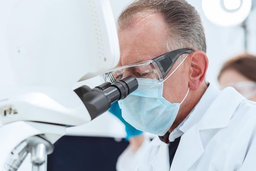 close up. scientist in a protective mask looking through a microscope. science and health protection.