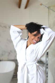 Young beautiful afro american woman wearing white bathrobe and dancing in hotel bathroom with marble walls. Concept of morning relax.