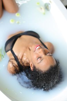 Young afro american woman relaxing in bathroom and wearing swimsuit. Concept of milk bath shoot and spa.