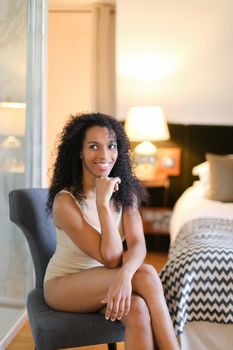 Young afro american woman sitting in room and wearing beige swimsuit. Concept of hotel photo session in lingerie.