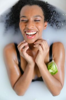 Portrait of cheerful afro american woman taking milk bath and wearing swimsuit. Concept of spa photo shoot and aromatherapy.