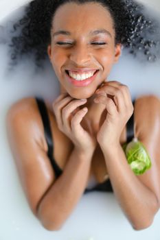 Portrait of happy afro american woman taking milk bath and wearing swimsuit. Concept of spa photo shoot and aromatherapy.