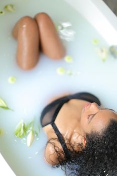 Afro american woman relaxing in bathroom and wearing swimsuit. Concept of milk bath shoot and spa.