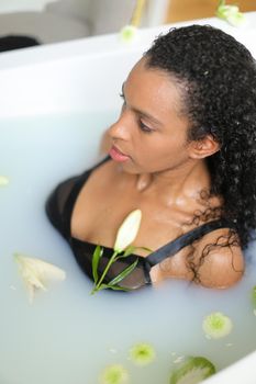 Portrait of afro american woman taking milk bath and wearing swimsuit. Concept of visiting spa and bathroom photo shoot.