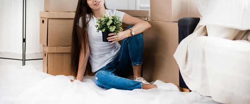 young woman with a home plant sitting on the floor in the new living room. photo with copy-space