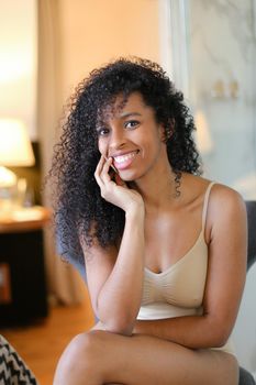 Young cute afro american woman sitting in room and wearing beige swimsuit. Concept of hotel photo session in lingerie.