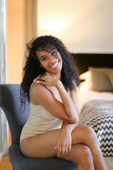 Young nice afro american woman sitting in room and wearing beige swimsuit. Concept of hotel photo session in lingerie.