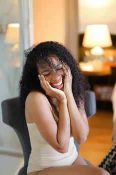 Young cheerful afro american woman sitting in room and wearing beige swimsuit. Concept of hotel photo session in lingerie.