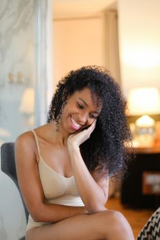 Young pretty afro american woman sitting in room and wearing beige swimsuit. Concept of hotel photo session in lingerie.