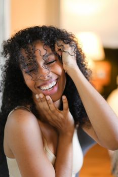 Portrait of beautiful smiling afro american woman sitting in room and wearing beige swimsuit. Concept of hotel photo session in lingerie.
