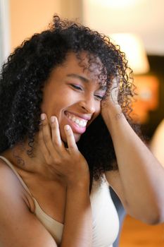 Portrait of young smiling afro american woman sitting in room and wearing beige swimsuit. Concept of hotel photo session in lingerie.
