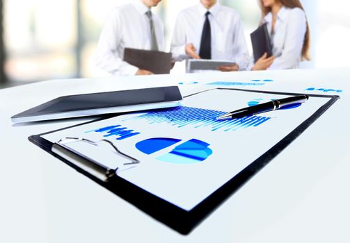 Close-up of business document in touchpad lying on the desk, office workers interacting in the background