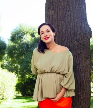 young pretty brunette pregnant woman outdoor in green park happy smiling, lifestyle people concept close up