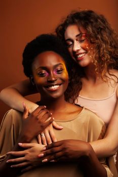 two pretty girls african and caucasian blond posing cheerful together on brown background, ethnicity diverse lifestyle people concept close up