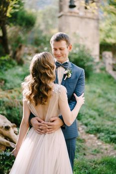 Groom hugs bride waist against the background of the old chapel in the garden. High quality photo