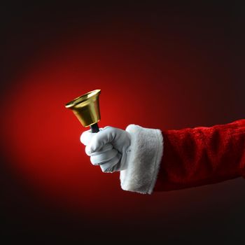 Santa Claus ringing a bell over dark red background. Square Format, only hand and arm are visible.