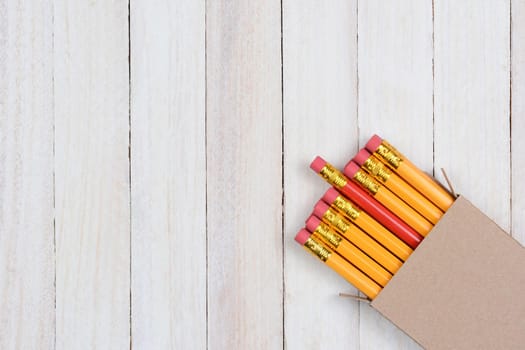 A box of yellow pencils with one red pencil partially pulled out. The plain brown box is in the lower right corner of the frame at an angle. 