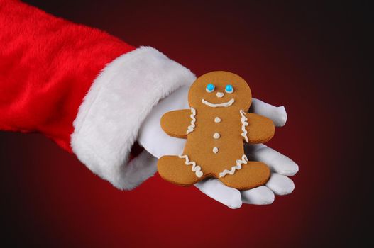 Santa Claus holding a Gingerbread man cookie in the palm of his hand. Horizontal format over a light to dark red background, showing only hand and arm.