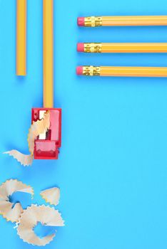Back to School Concept: Yellow Pencils with a sharpener and shavings, on a blue background. Three pencils with eraser end entering the frame from the top right side with copy space below.