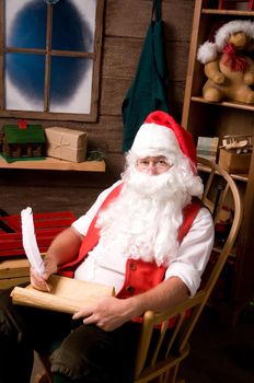 Santa Claus sitting in his workshop making notes on his naughty list with a quill pen. Vertical Composition.