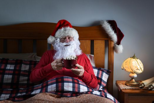 Santa Claus sitting in bed with a large mug of hot cocoa before he goes to sleep on Christmas Eve.