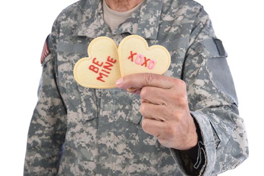 Closeup of a soldier holding two Heart Shaped Valentines Day cookies in one hand with the words Be Mine and XOXO written in red icing.