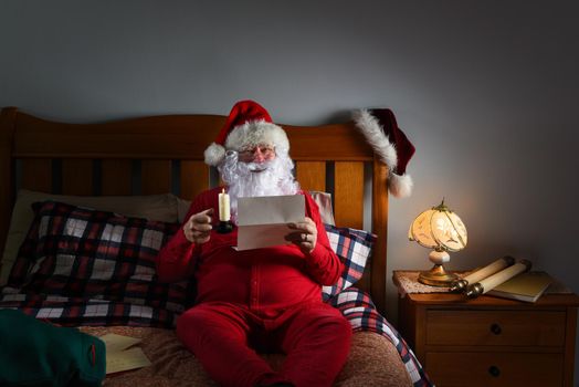 Santa Claus in his red long johns reading letters by candlelight on top of his bed at the North Pole.