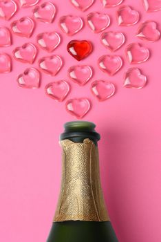 Valentines Day Concept: high angle shot of a white champagne bottle with pink glass hearts simulating a spray.