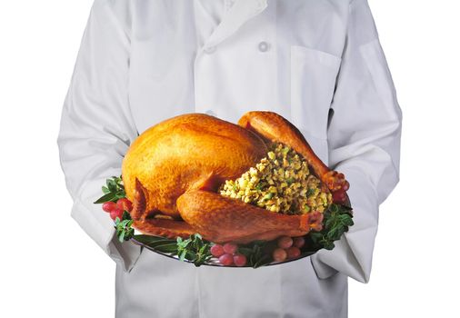 Closeup of a chef holding a Thanksgiving Turkey on a platter with garnish. Man is unrecognizable, on a white background.