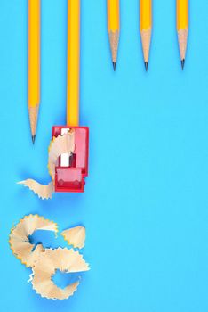 Back to School Concept: Five Yellow Pencils with a sharpener and shavings, on a blue background. Three sharpened pencils partially into frame at the top right with copy space below.