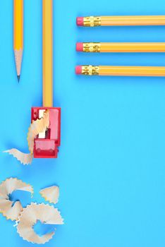 Back to School Concept: One Yellow Pencil with a point and a sharpener and shavings, on a blue background. Three pencils with eraser end enter the frame from the top right side with copy space below.