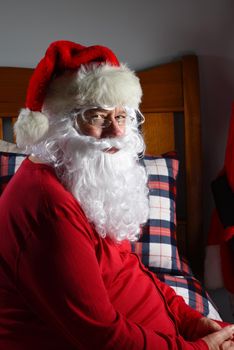 Closeup of  Santa Claus sitting on his bed in his red long johns, ready for sleep after Christmas.