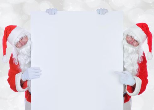 Two Santa Claus on either side of a large blank sign. Both men are holding on to the paper and one is pointing at blank space. 