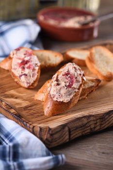 Delicate chicken pate with mashed cranberries spread on toasted baguette slices. Country style food.