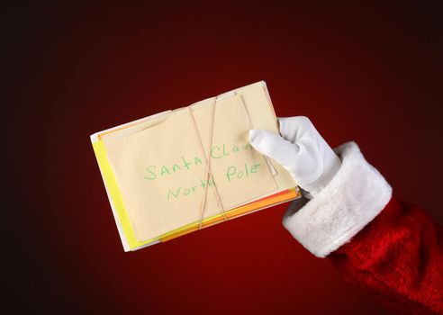 Closeup of Santa Claus holding a bunch of letters bound with a rubber band. Horizontal format on a light to dark red spot background.