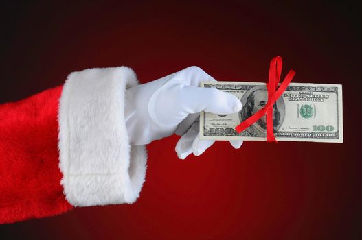 Santa Claus hand with cash tied up with a red ribbon. Horizontal format over a light to dark red background.