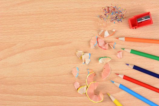 High angle view of six colored pencils on a school desk with a sharpener and shavings. Horizontal with copy space. Back to school concept.